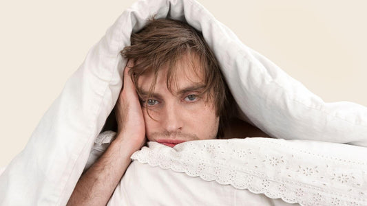 A man under blankets looking tired, representing the theme of What Helps Americans Sleep Best?